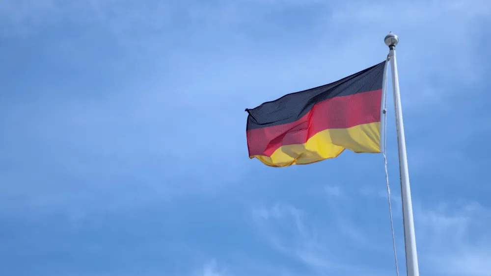 Deutsche Nationalflagge weht an einem weißen Mast vor blauem Himmel